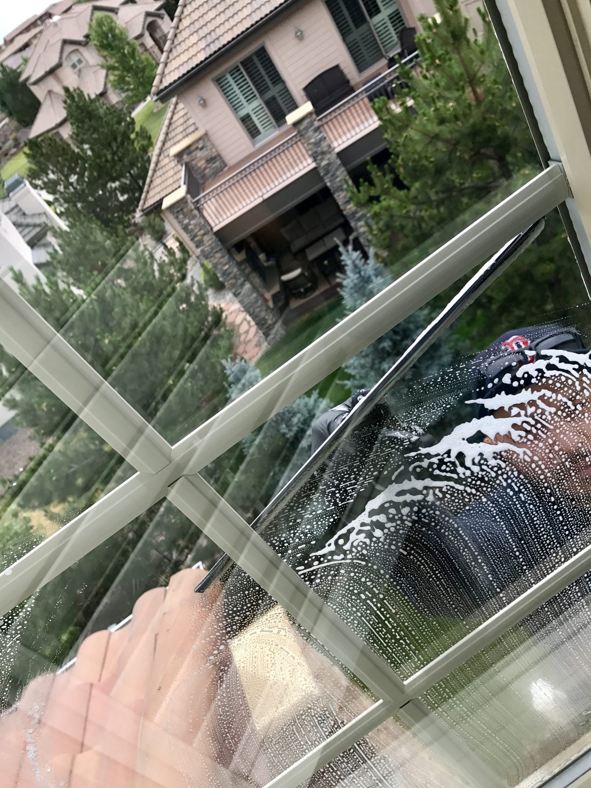 Before and after: Denver Pros technician squeegeeing a soapy window to a streak-free finish at an Aurora, CO home